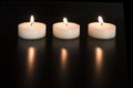 Three burning tea lights in line with their reflection on a black background Royalty Free Stock Photo