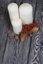 Three white candles stand on painted pine planks. Nearby are spruce cones, dried rowan berries and acorns Royalty Free Stock Photo