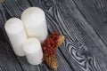 Three white candles stand on painted pine planks. Spruce cones and dried rowan berries are laid out nearby Royalty Free Stock Photo