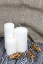 Three white candles stand on painted pine planks. Spruce cones are spread out nearby Royalty Free Stock Photo