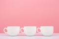 Three white ceramic cups in a row on white table against pink background Royalty Free Stock Photo