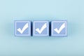 Three white checkmarks on blue cubes against bright pastel blue background