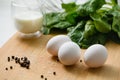 Three white chicken eggs on a cutting board with a bunch of fresh spinach Royalty Free Stock Photo