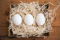 Three white eggs in the hay nest, wooden background