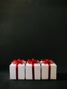 Three white gift boxes together with red bows on black background. Vertical.