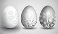three white and gray easter eggs with floral designs on the sides of them, on a gray background, with a shadow of the egg Royalty Free Stock Photo