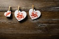 Three white hearts with discounts hang on the clothespins on the rope on brown wooden background. Big sale