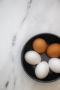 Three white Organic Eggs with Two Organic Brown Egg in a black Bowl on a Marble Counter Top