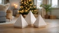 Three white paper pyramids on a table with a decorated Christmas tree in the blurred background. Royalty Free Stock Photo
