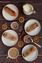 Three white plates with cakes, a cup of coffee, sugar, cinnamon sticks, orange slices and milk on a dark wooden table Royalty Free Stock Photo