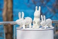 Three white rabbit statues made of plaster on barrel at outdoor art exhibition, artificial hares