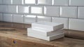 Three white rectangular boxes stacked on a wooden surface. The background features a wall with white subway tiles, creating a Royalty Free Stock Photo