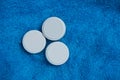 Three white round pills on blue woolen fabric background Royalty Free Stock Photo