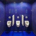 Three white urinals in men public toilet against blue wall. Royalty Free Stock Photo