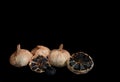 three whole bulbs of black fermented garlic and one cut crosswise isolated on black Royalty Free Stock Photo