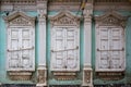 Three windows with closed shutters of an old house with carved decor and stucco, a fragment of the facade