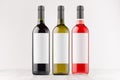 Three wine bottles - red, green, black - with blank white labels on white wooden board, mock up.