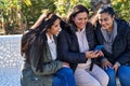 Three woman mother and daughters using smartphone sitting on bench at park