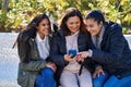 Three woman mother and daughters using smartphone sitting on bench at park