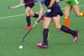 Three women battle for control of ball during field hockey game