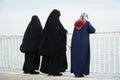 Three women in a burqa look at the sea