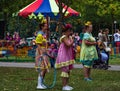 Three women in clown costumes stand on green grass in the park
