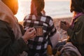 Three women female friends having picnic, drinking hot tea from iron mugs, sitting on beach Royalty Free Stock Photo