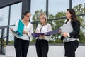 Three women with folders standing outside building and looking in documents Royalty Free Stock Photo