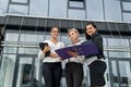 Three women with folders standing outside building and looking in documents Royalty Free Stock Photo