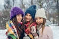 Three women friends outdoors in knitted hats having fun on a snowy cold weather. Group of young female friends outdoors