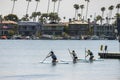 Three women rowing paddle boards on the blue ocean water with luxury homes and boats and yachts docked along the banks