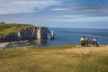 Three women sit on a bench and look at dark blue water and the chalk cliffs with arch