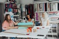 Three women collaborate in sewing studio surrounded by colorful threads fabrics textile rolls and sewing supplies while Royalty Free Stock Photo