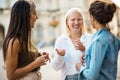 Cheerfully talk. Three women standing on street and talking. Focus is on blond woman