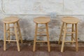 Three wooden barstools against a concrete cement wall in a basement