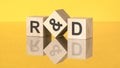 three wooden blocks with acronym R and D on yellow background. reflection of an image on a glass surface concept