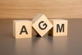 three wooden blocks on a brown background, with the abbreviation AGM - Annual General Meeting