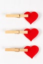 Three wooden clothespins with a metal spring hold a red heart on a white wooden table background Royalty Free Stock Photo