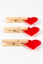 Three wooden clothespins with a metal spring hold a red heart on a white wooden table background. close-up. Royalty Free Stock Photo