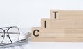 Three wooden cubes with letters CIT on the white table with keyboard and glasses