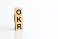 Three wooden cubes with letters OKR - Objectives and Key Results, on white table, more in background, space for text in right down