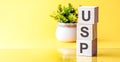 Three wooden cubes with letters - USP - on yellow table, front view concepts, flower in the background Royalty Free Stock Photo