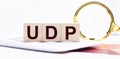Three wooden cubes with the text UDP User Datagram Protocol stand on a white calculator near a magnifying glass. Business concept