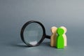 Three wooden human figure stands near a magnifying glass on a gray background. The concept of the search for people and workers.