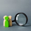 Three wooden human figure stands near a magnifying glass on a gray background. The concept of the search for people and workers Royalty Free Stock Photo