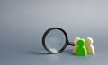 Three wooden human figure stands near a magnifying glass on a gray background. Human resources, management.