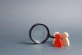 Three wooden human figure stands near a magnifying glass on a gray background. Search for vacancies and work. Human resources