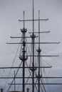 Three wooden masts of a Dutch fluyt merchant sailing ship of XVIII century on a grey sky and clouds background vertical close up