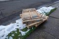 Three wooden pallets stacked on each other on snow covered grass next to a street