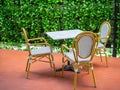 Three wooden white vintage chairs with white marble table on red floor on green ivy plant background Royalty Free Stock Photo